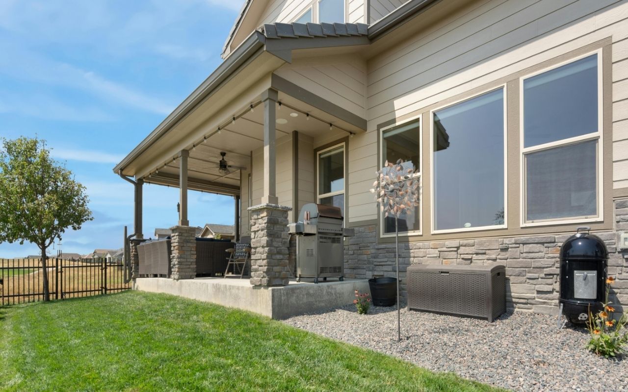 Modern beige and gray home exterior with vinyl siding and stone accents, featuring a covered patio and clean landscaping